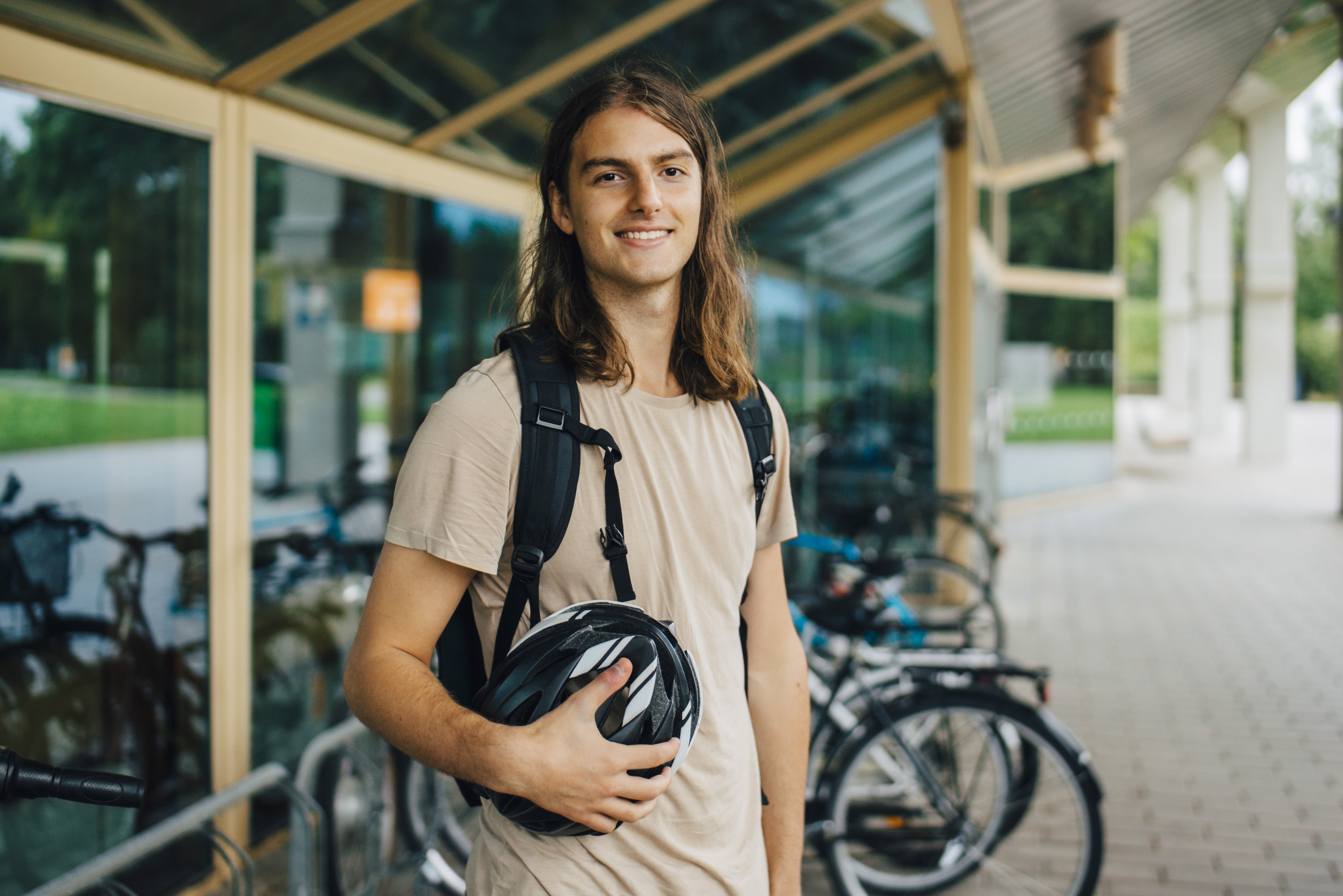 Ung man står framför en cykelparkering, ler och håller i en cykelhjälm