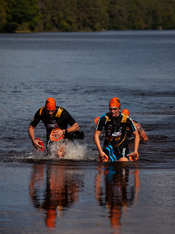 Två tävlande springer i vattnet under Blackwater Swimrun.